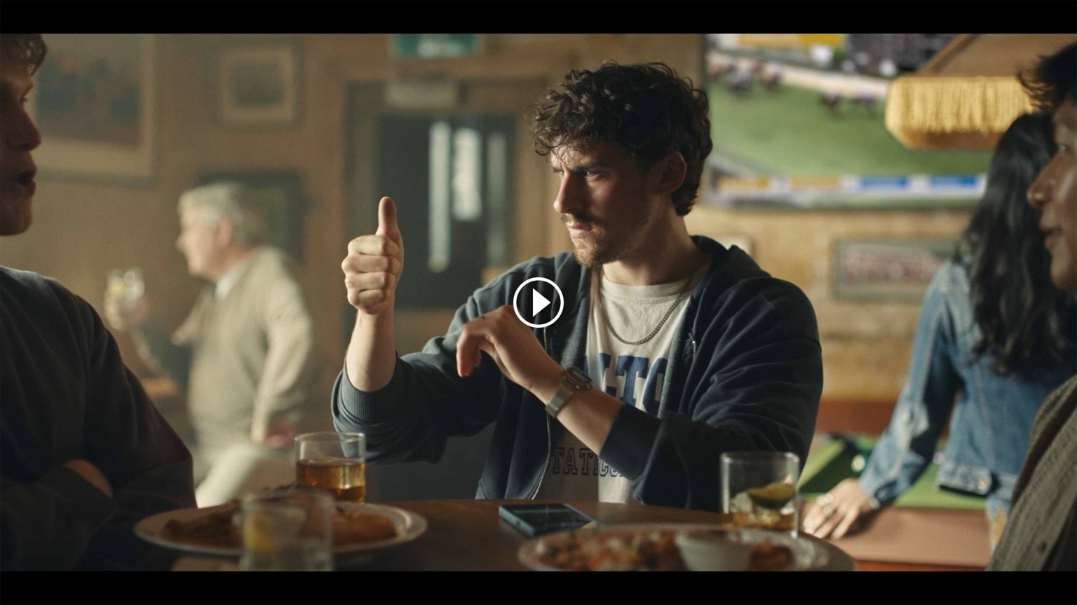 A young male in a pub is looking at this thumb at eye level with a look of confusion